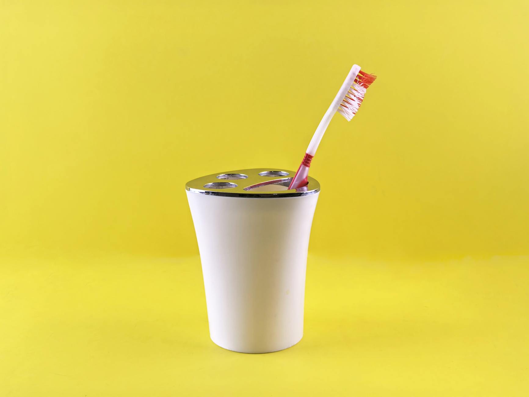 Czerwona szczoteczka w białym kubku na żółtym tle