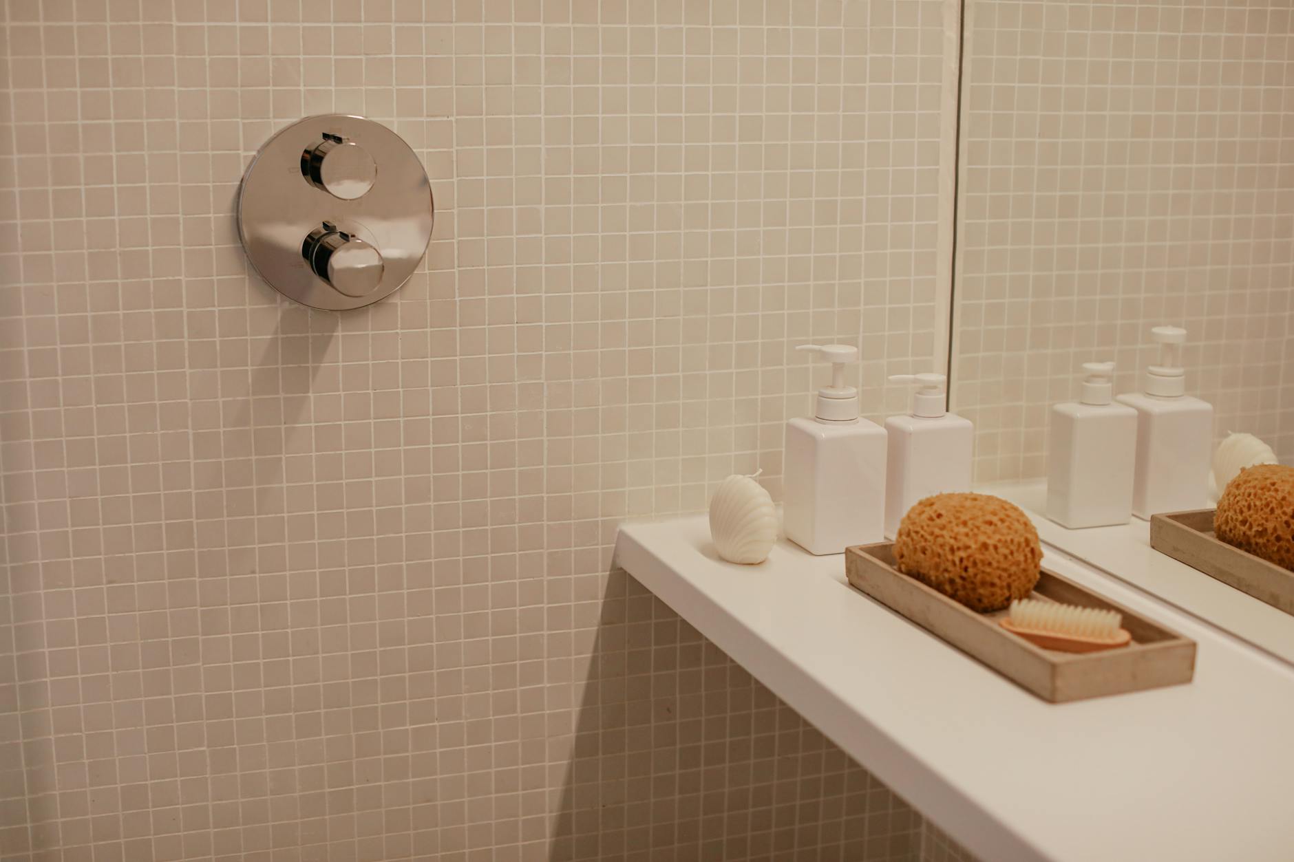 Minimalistyczna łazienka z dozownikami mydła i gąbką na półce