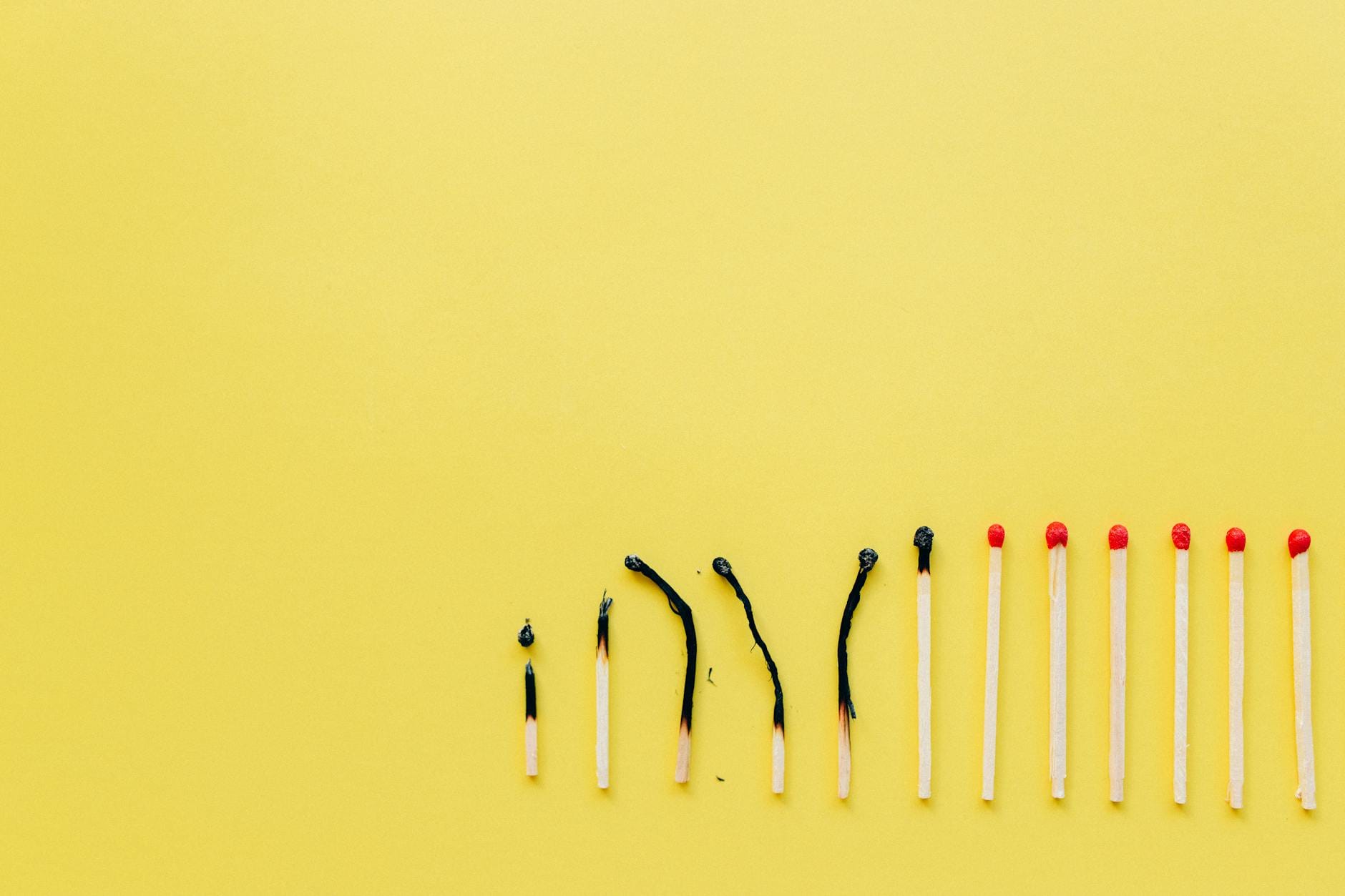 Rząd spalonych i nienaruszonych zapałek na żółtym tle