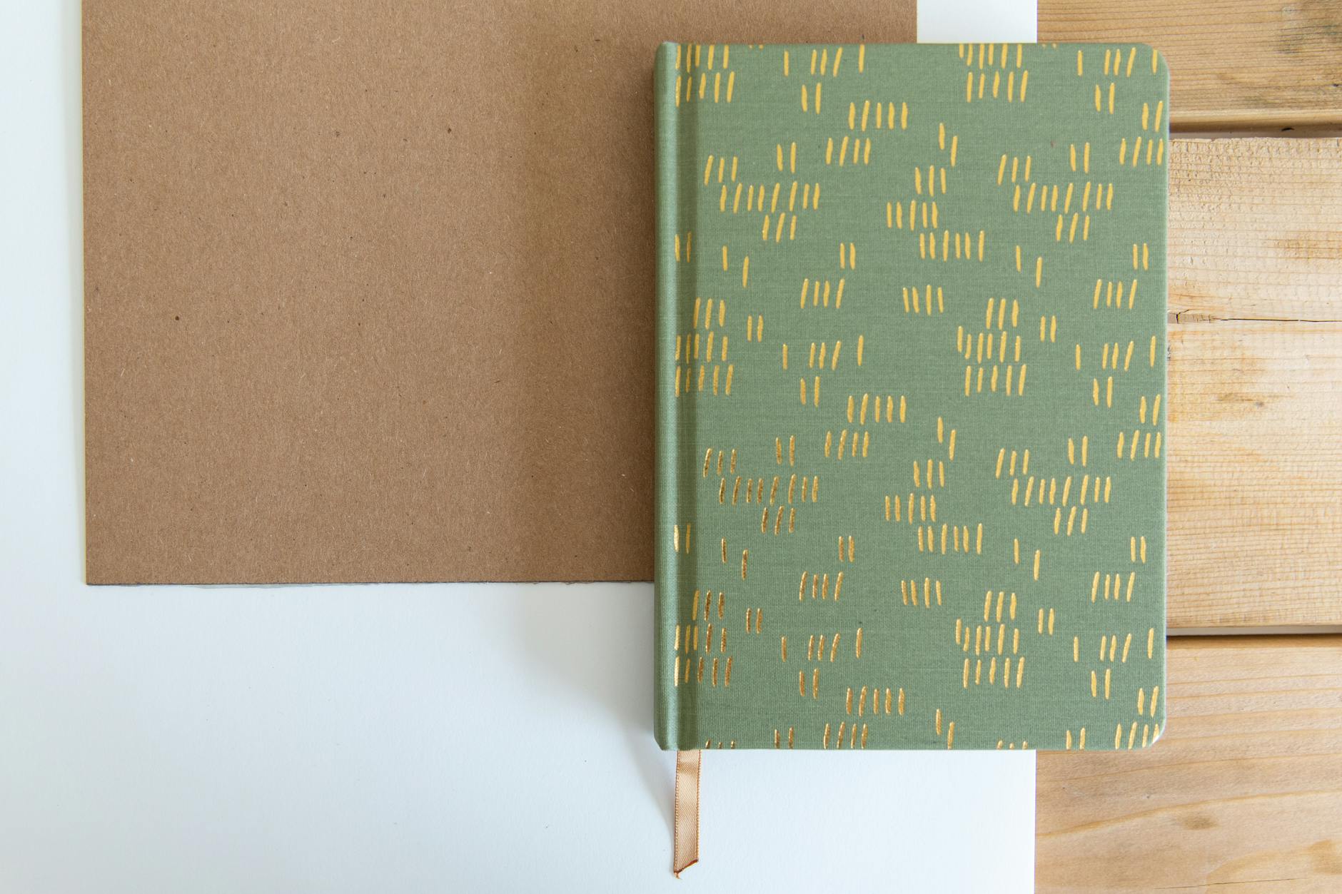 Zielony notes w motywy roślinne na biurku z kartonem i białymi kartkami