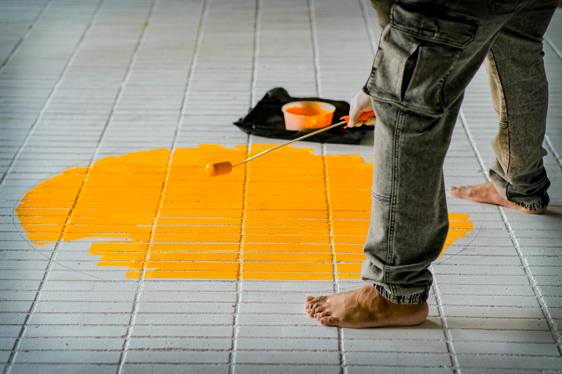 Bosą stopą maluje żółte koło wałkiem na białych płytkach kuchennych