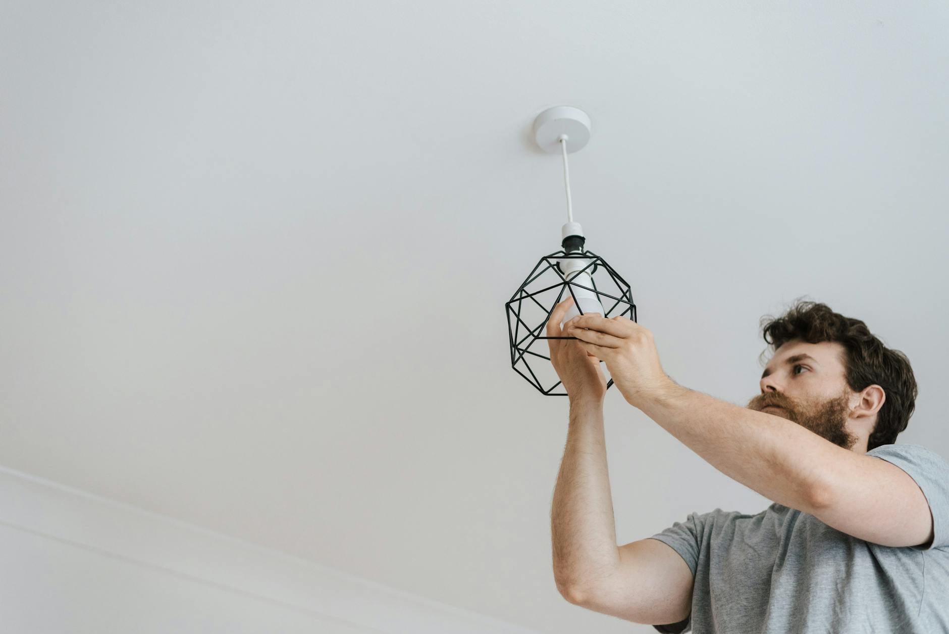 Mężczyzna wkręca żarówkę do nowoczesnej lampy sufitowej