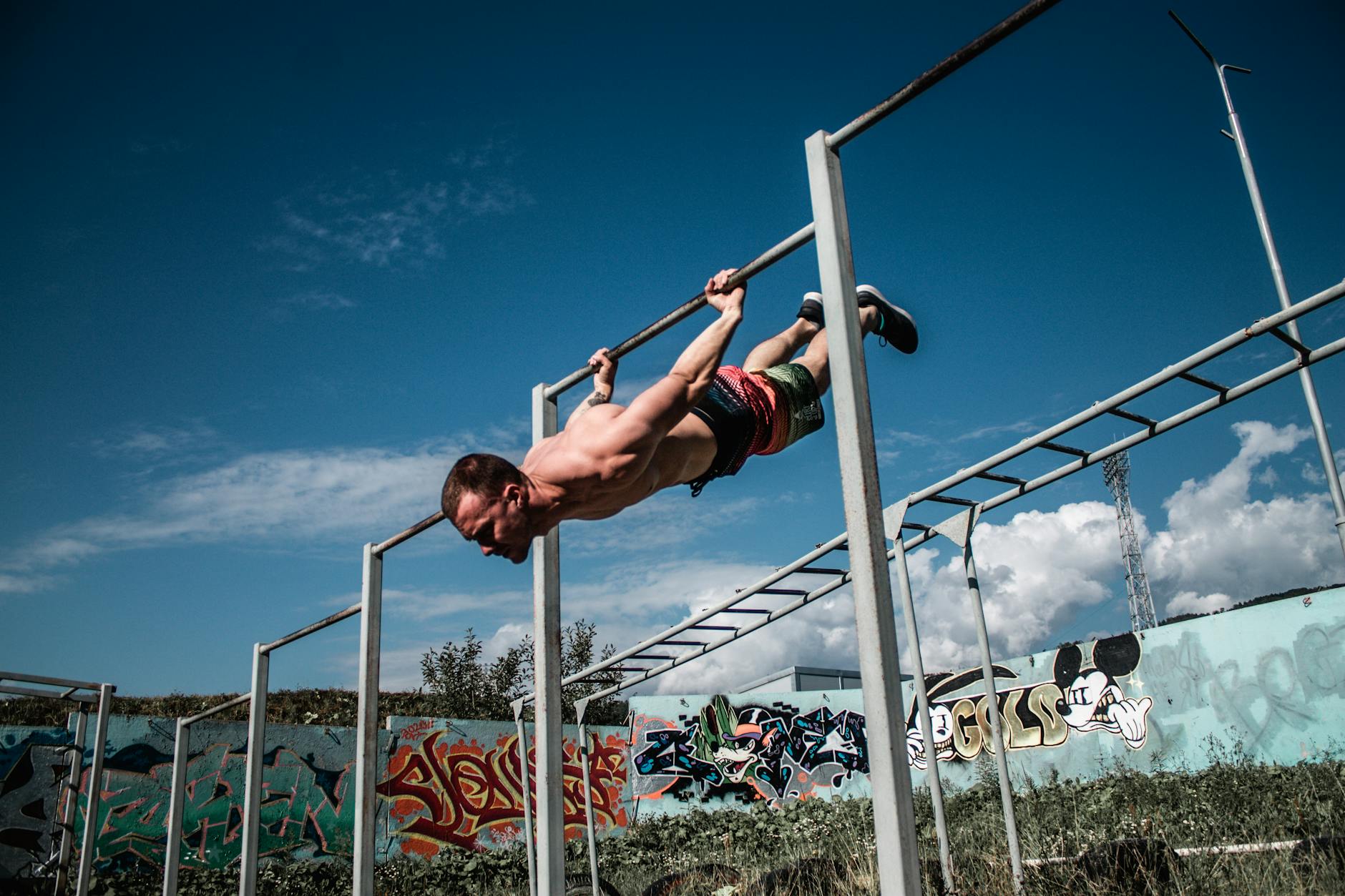 Mężczyzna wykonuje human flag na drążkach street workout przed graffiti