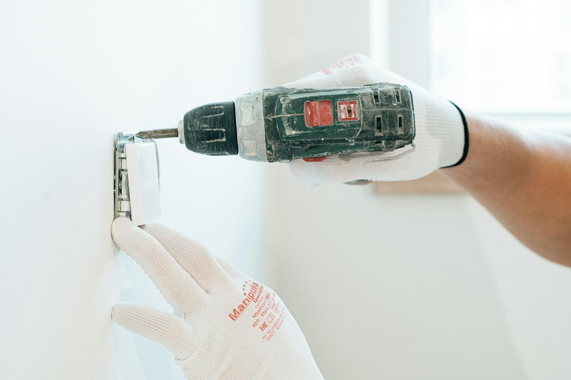 Montaż gniazdka w ścianie w rękawicach ochronnych za pomocą wiertarki